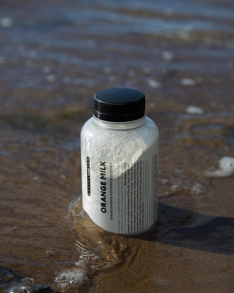 Close-up of a powdered milk bottle on a sandy beach at the water's edge.