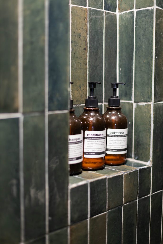 Elegant amber bottles of shampoo, conditioner, and body wash in a modern, tiled shower.