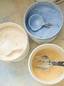 From above of white plastic containers with multicoloured dental material with metal scoops inside placed on floor in dental laboratory